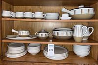 Full view of Denby dishes including mugs, saucers, plates, bowls, teapot, pitcher, tureen, platter on wooden shelves