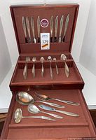 Open wood chest displaying Firelight pattern flatware with knives, forks, spoons and serving pieces.
