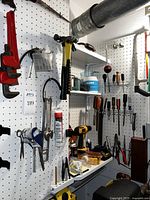 General overview of hand tools hanging on pegboard and shelf, showing power drill, drill charger, and hand tools.