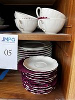Stack of white china plates with scalloped edges and teacups on shelf