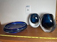 Photo of the pair of blue vases with blue glass candy dish on a wooden shelf with a measuring tape showing size.
