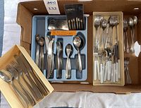 Overhead view of cardboard box containing blue plastic organizers filled with assorted stainless steel flatware pieces