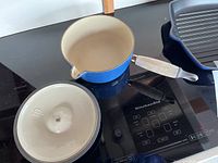 Saucepan interior, lid removed, showing cream-colored enamel and wooden handle