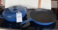 Photo of blue Le Creuset braiser with lid on left and black cast iron fry pan on right on stovetop.