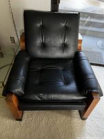 Front view of black leather tufted armchair showing exposed tenon wood frame
