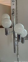 Chrome hanging light fixture with 5 white globe bulbs and metal swag chain shown from the side angle.