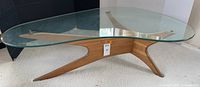 Front view of entire coffee table showing kidney-shaped glass top and walnut tri-leg base