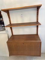 Front view of entire wall-mounted shelving unit showing two shelves above drop-down cabinet