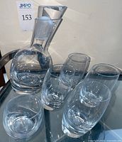 Full view of the Nambé full lead crystal tilt decanter and the five glasses arranged on a surface.