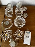 Overview of all crystal candle holders in the lot on a wooden surface including the cube candle holders, raspberry shaped votive holder, round tea light holder, star shaped holders and smaller items.