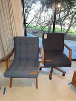 Photo showing both chairs side by side, the office chair on wheels with blue upholstery and wooden arms on the right and the MCM lounge chair with button tufted blue fabric upholstery and wooden arms on the left.