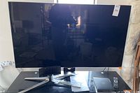 Samsung 55 inch flat screen television on black table with remote and box nearby.