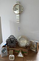 Wide view showing the entire selection of clocks including the Seiko wall clock on the wall, Howard Miller clock on the box, decorative gears clock on the right, and five smaller desk clocks grouped at the bottom.