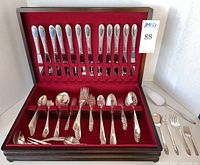 Full wooden storage chest with red felt interior containing the complete flatware set for 12, including knives, forks, spoons, and five additional serving pieces laid to the side.