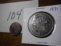 Front side of 1971 large commemorative coin and smaller cent coin showing shield and floral elements with date 1971.