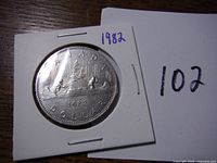 Reverse of the 1982 Canadian Voyageur silver dollar showing the voyageur canoe design with two paddlers and date 1982.