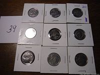 Nine commemorative quarters in individual holders arranged in a 3x3 grid on a wooden surface with a card showing number 39.