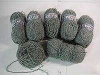Seven skeins of denim colored wool yarn arranged in two rows with one skein partially unwound.