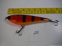 Top-side view of the orange and black striped musky and pike bait lure with a measuring tape for scale showing it is about 6.5 inches long.