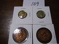 Four replica Roman coins in protective holders, arranged on wooden surface with lot number 109 visible.