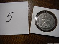 Close-up image of the King George VI silver-colored medallion showing the crowned profile and inscription, with a paper labeled '5' visible.