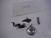 Four silver charm and pendant items displayed together on white background with a card labeled '145'