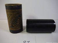 Photo showing the black cylindrical record next to its cylindrical paper label case with visible text indicating it is a 2-minute Indestructible Record.