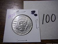 Reverse of 1973 Kennedy Half Dollar Coin in cardboard holder showing presidential eagle seal and denomination.