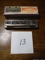 Top view of the Marine Band harmonica showing embossed trademarks, model number, and original box with brand name and illustration.