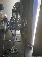 Photo of a black back stretcher with ergonomic design, adjustable support, and two black cushions placed on a wooden floor near a window.