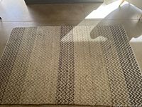 Rectangular woven area rug laid flat on floor with visible natural light and shadow.
