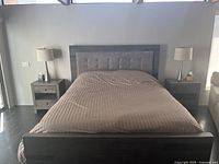 Photo of bedroom set showing bed with upholstered headboard flanked by two matching end tables and two table lamps