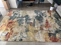 Photo showing rectangular multicolor abstract rugs with a distressed design in colors such as green, beige, yellow, red, and blue placed on a light floor in a living room setting.