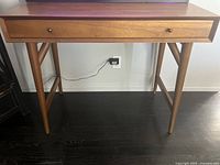Photo of a mid-century style wooden desk with a single drawer, tapered angled legs, and two round knobs
