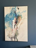 Full view of large abstract painting with blue, black, white, pink, brown, and green colors on a canvas hung on a blue wall.