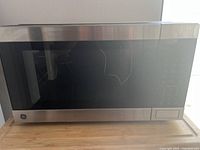 Front view of stainless steel General Electric microwave/air fryer unit showing large black glass door with control panel on the right side.