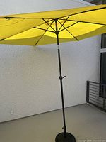Yellow patio umbrella fully opened, showing the fabric canopy and black metal pole structure.