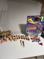 Wide view of the assortment of colorful McDonald's character toys on wheeled vehicles arranged in a row in front of the large Giant Game electronic board game box.