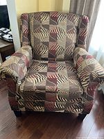 Front view of the accent chair showing the patterned upholstery, cushioned seat, armrests, and wooden legs.