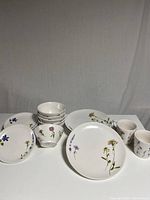 Full set of dishes showing side plates, bowls, dinner plates, mugs with floral designs.