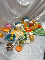 Full view of Fisher Price Fun With Food set showing kitchen appliances, plates, utensils, cups, placemat, and play food items arranged on white fabric background.