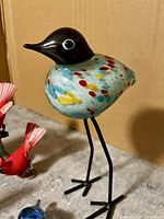 Close-up of multicolored ceramic bird with black head and wire legs