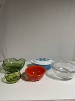 Front view of all items: Pyrex casserole dish with opal lid (blue and white floral), clear nesting bowls with etched flowers, red-orange mixing bowl, and green chip and dip bowls