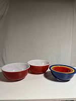Image showing two large red Pyrex bowls and four multicolored nesting bowls stacked together.