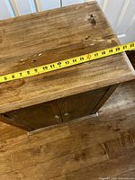 Top view of solid walnut cabinet showing measurement tape indicating approximately 23 inches in width, with visible wear and marks on the wood surface.