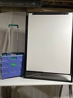 White tabletop dry erase board and blue and green carrying cart with telescoping handle, shown side by side on a table.