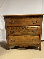 Front view of the vintage wooden dresser showing three drawers with metal pull handles and keyholes on the top and bottom drawer.