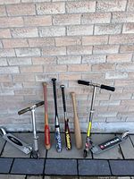 Wide photo showing four baseball bats and two scooters against brick background