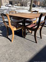 Vintage wood dining table with collapsible sides shown fully extended with four chairs around it placed outdoors on pavement with snow in background.
