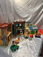 Wide view of vintage Fisher Price Sesame Street house and clubhouse playsets with assorted Little People figures and accessories on a white cloth backdrop.